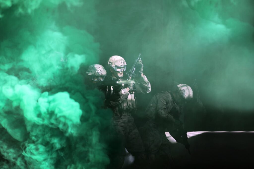Three soldiers emerge from green smoke in a tactical military operation.